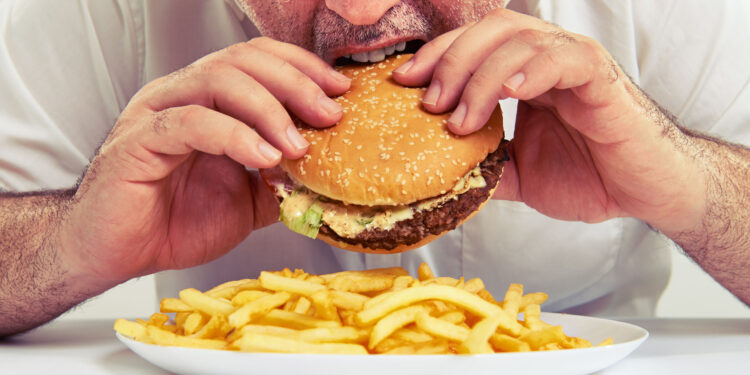 close up photo of man eating burger and french fries التوتر يزيد الوزن وهذه هي الاسباب