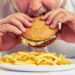close up photo of man eating burger and french fries التوتر يزيد الوزن وهذه هي الاسباب